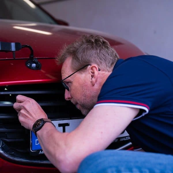 Gutachter / Sachverständiger leuchtet mit Taschenlampe in den Motorraum eines roten Fahrzeugs