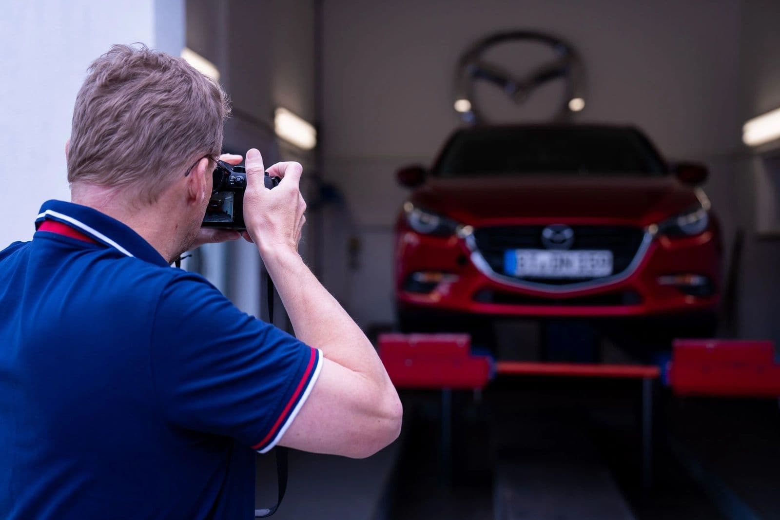 Kfz-Sachverständiger Stefan Krebs fotografiert ein rotes Fahrzeug auf der Hebebühne